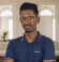 Man wearing glasses and a blue polo shirt standing indoors with blurred background.